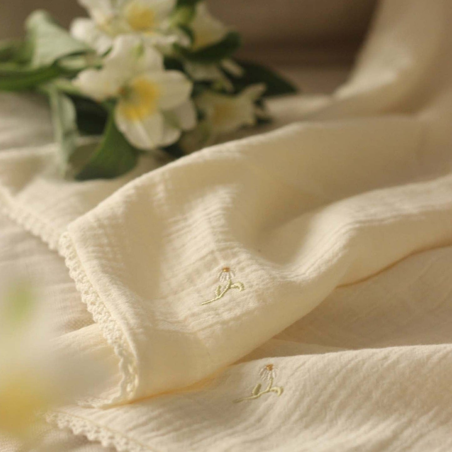 Close-up of beige fabric with floral embroidery, blurred flowers in the background