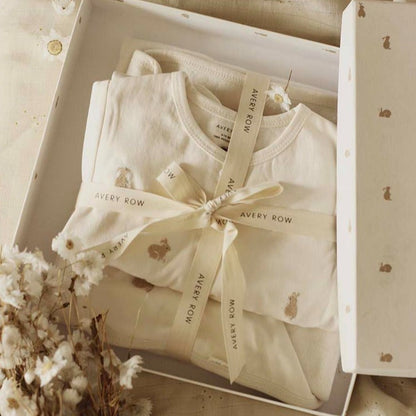 Baby outfit with a bow in a box, featuring 'Avery Row' branding, surrounded by decorative elements.