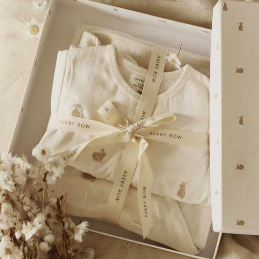 Baby outfit with a bow in a box, featuring 'Avery Row' branding, surrounded by decorative elements.