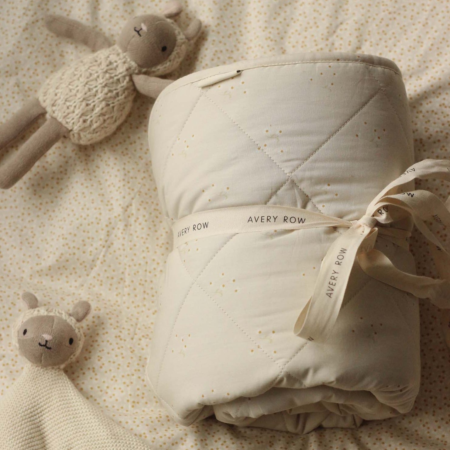 Folded baby blanket with 'Avery Row' label on a soft textured surface with plush toys.