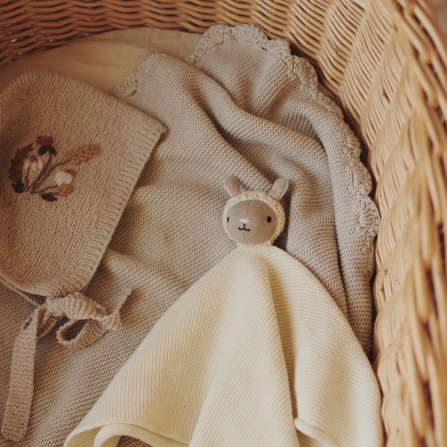 Baby bonnet and blanket with a soft toy in a wicker basket