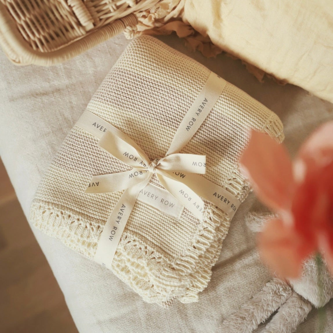 Beige textured blanket with a ribbon and 'Avery Row' label on a soft surface.