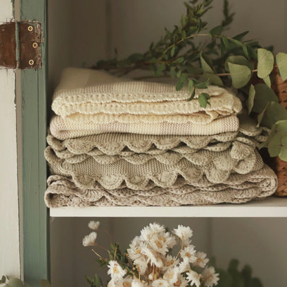 Stack of folded textured blankets on a shelf with greenery
