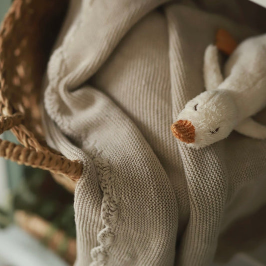 Close-up of a plush toy duck on a textured fabric surface with a blurred background