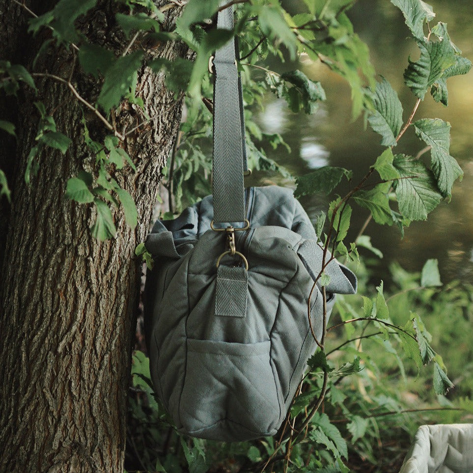 Green backpack hanging on a tree in a forest setting