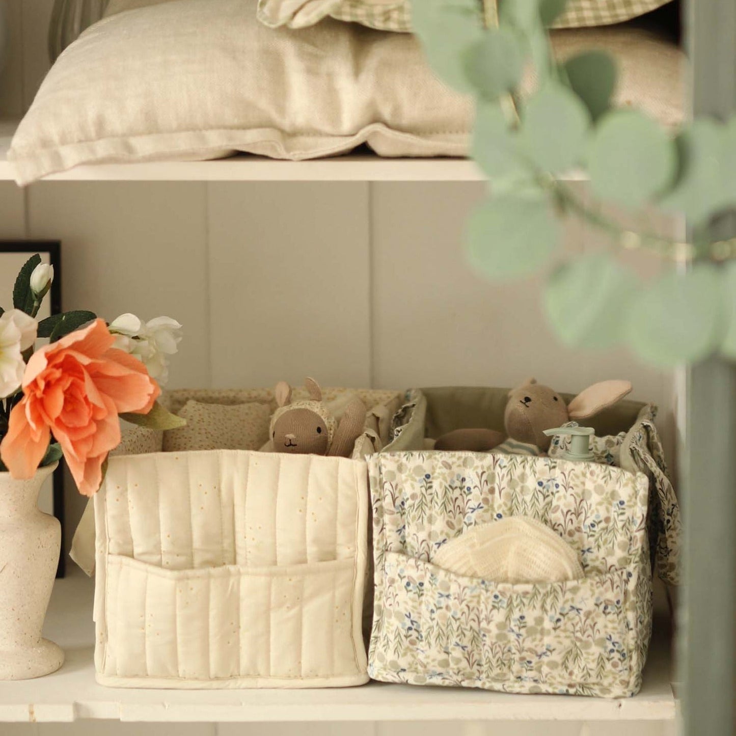 Two storage baskets with decorative items on a shelf, including a vase with flowers and a plant.