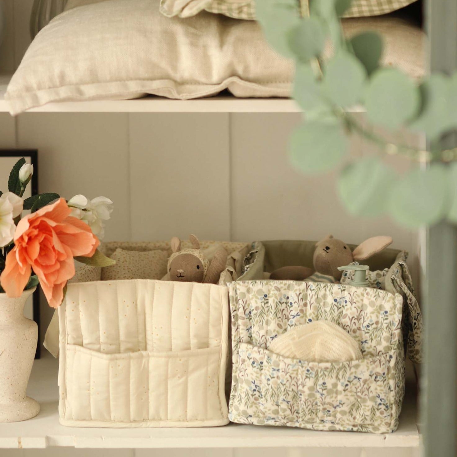 Two storage baskets with decorative items on a shelf, including a vase with flowers and a plant.