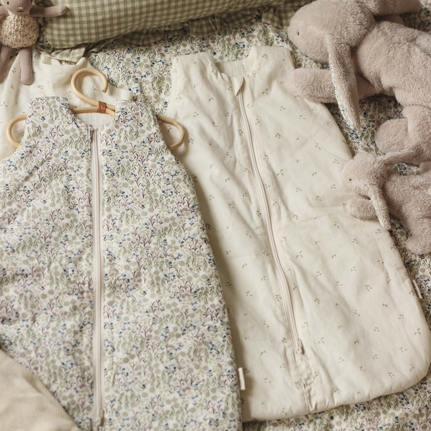 Two baby sleeping bags, one floral and one plain, on a textured surface with soft toys.