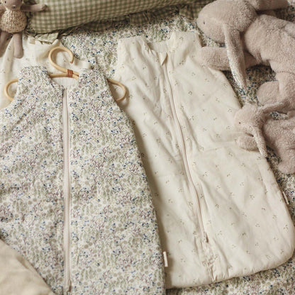 Two baby sleeping bags, one floral and one plain, on a textured surface with soft toys.