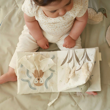 Baby sitting on a soft surface with a fabric book featuring animal illustrations.