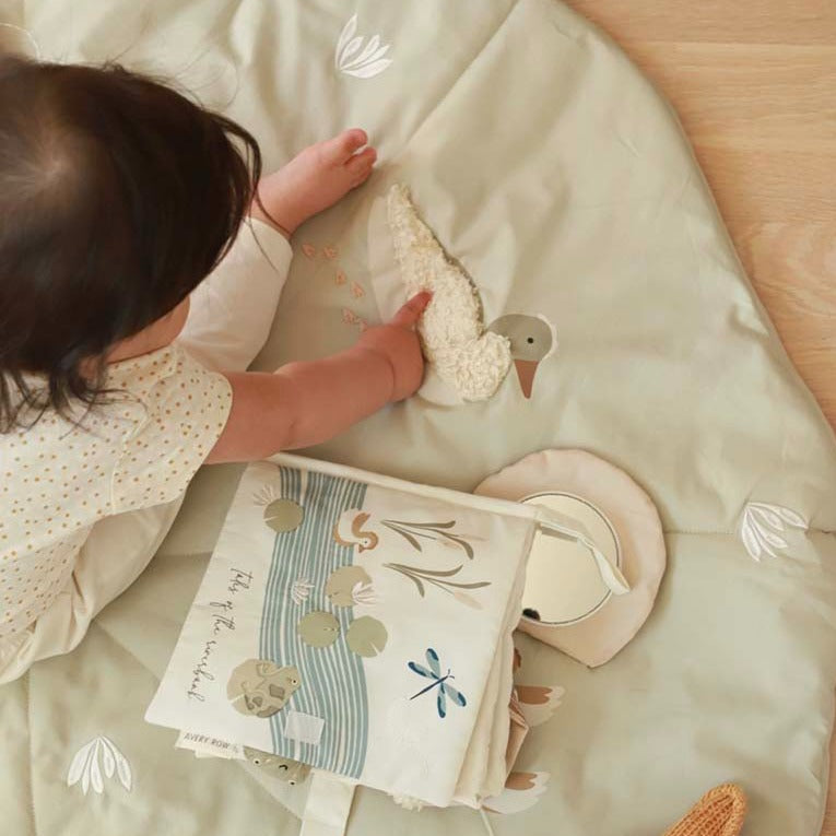 Child playing with a soft toy and book on a light green blanket