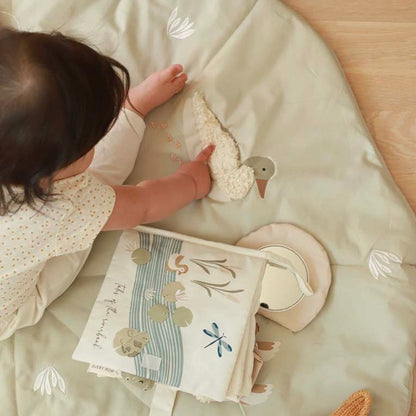 Child playing with a soft toy and book on a light green blanket