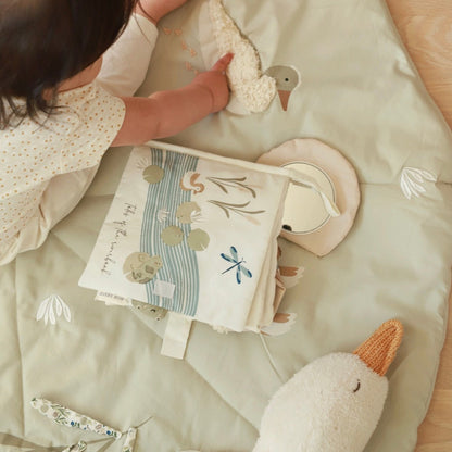 Child playing with a soft toy and book on a bed with a light green blanket