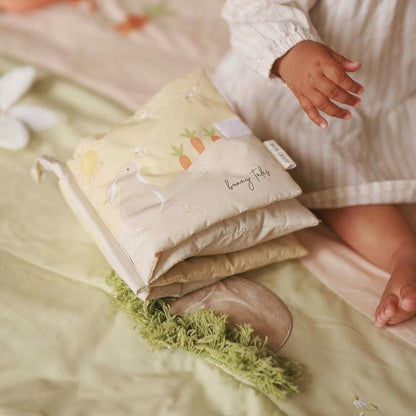 Stack of baby blankets with a child's hand reaching towards them on a soft surface.