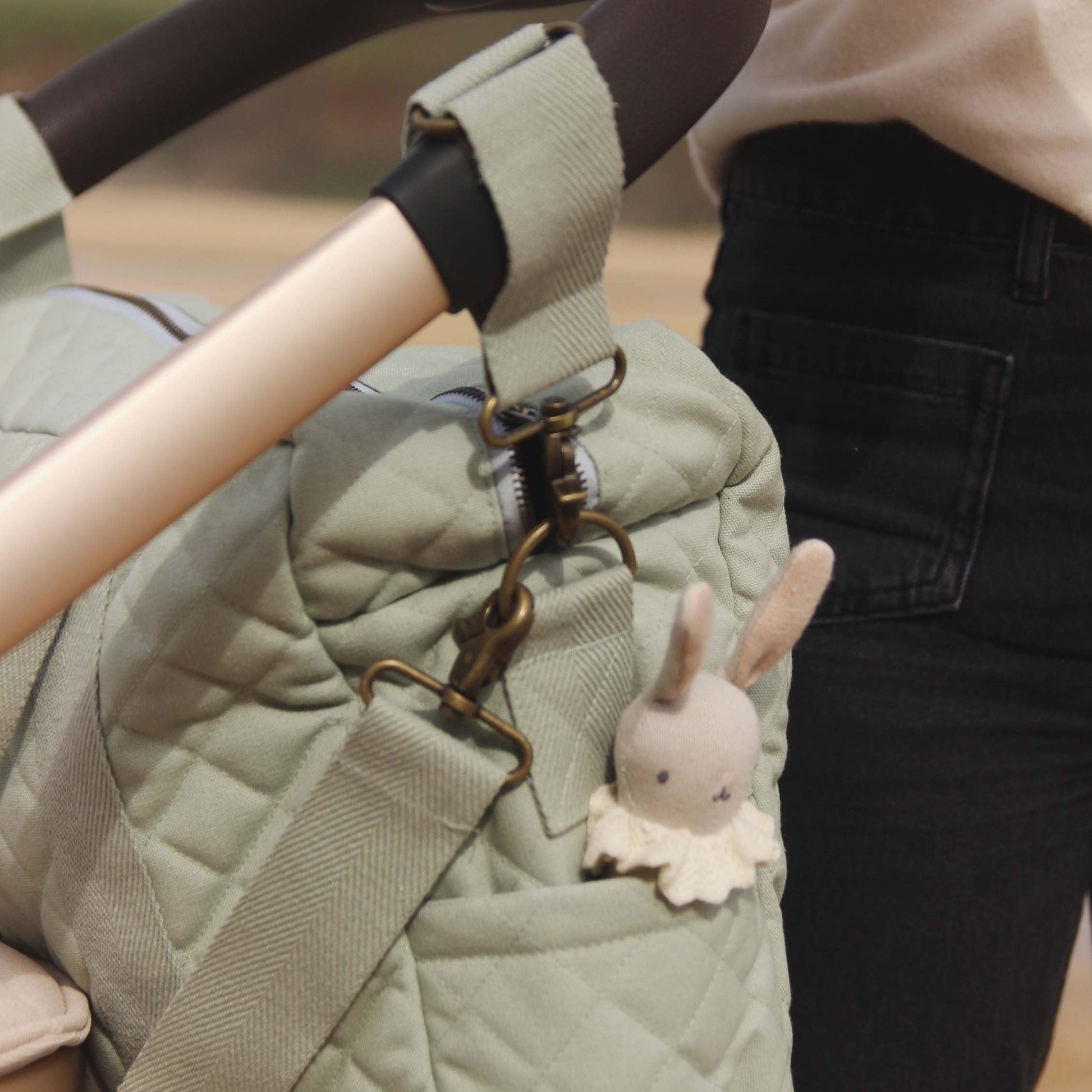 Green quilted bag with a rabbit charm attached, held by a person wearing black pants.