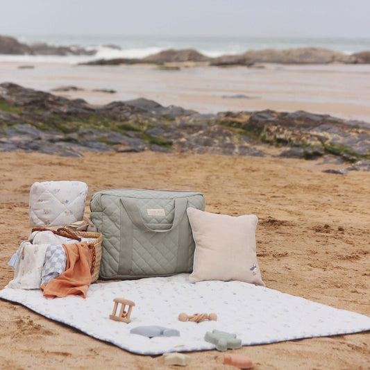 Outdoor setting with baby items on a blanket by the beach