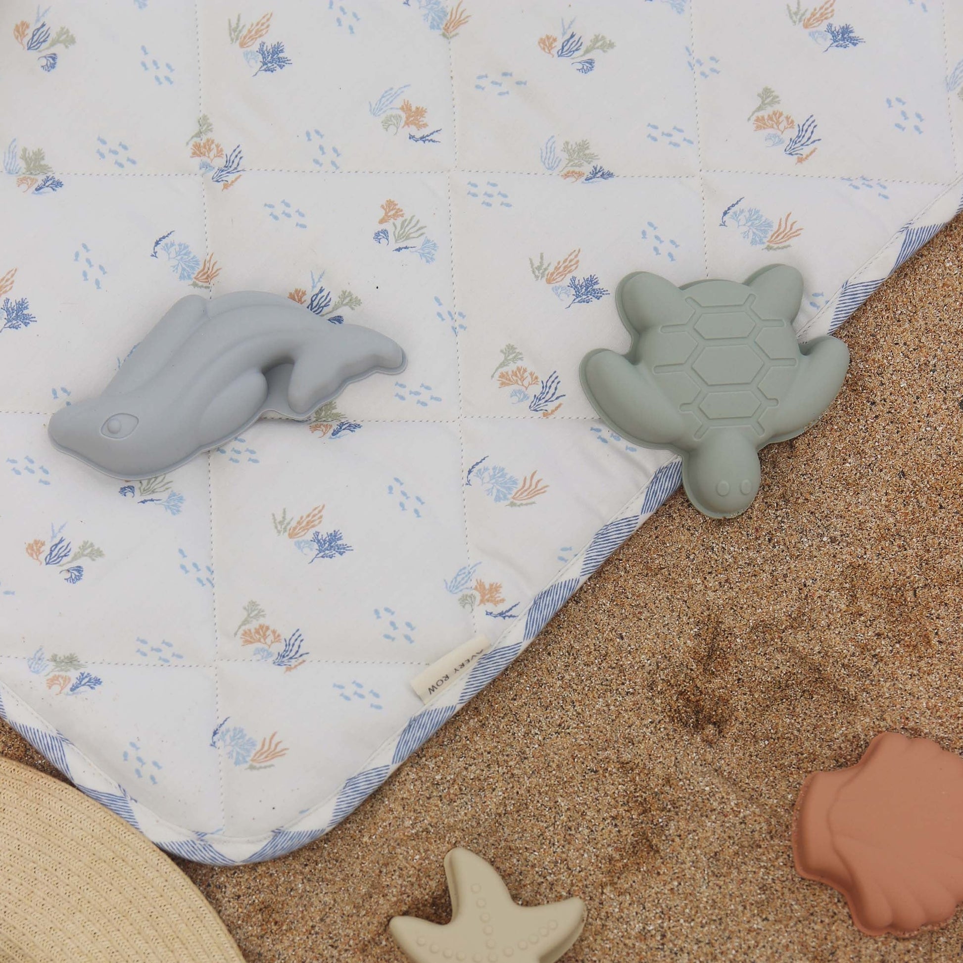 Toy turtle and shark on a patterned blanket with sand around