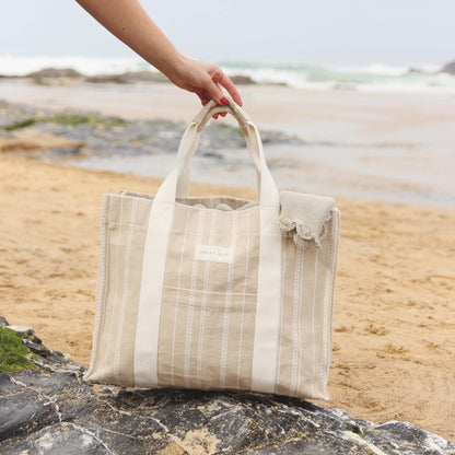 Beige tote bag held by a hand on a beach