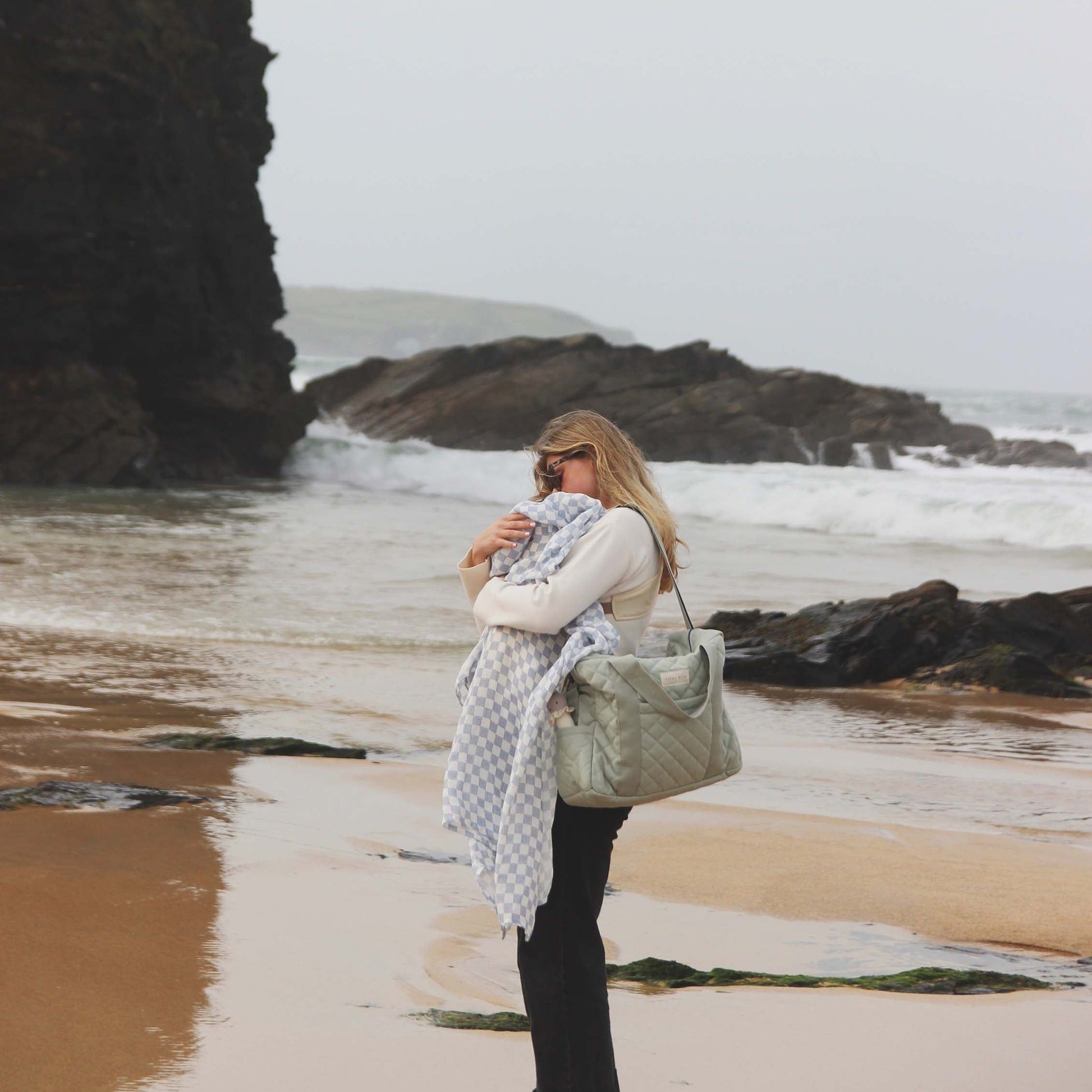 Woman standing on a beach with waves and rocks in the background