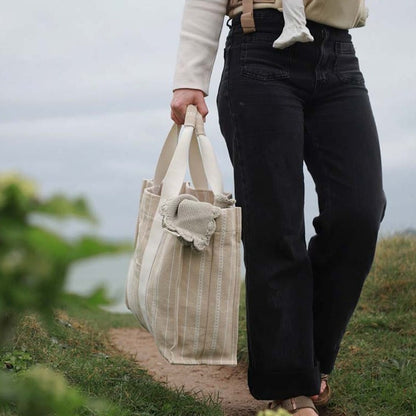 Person holding a beige tote bag outdoors with a blurred background