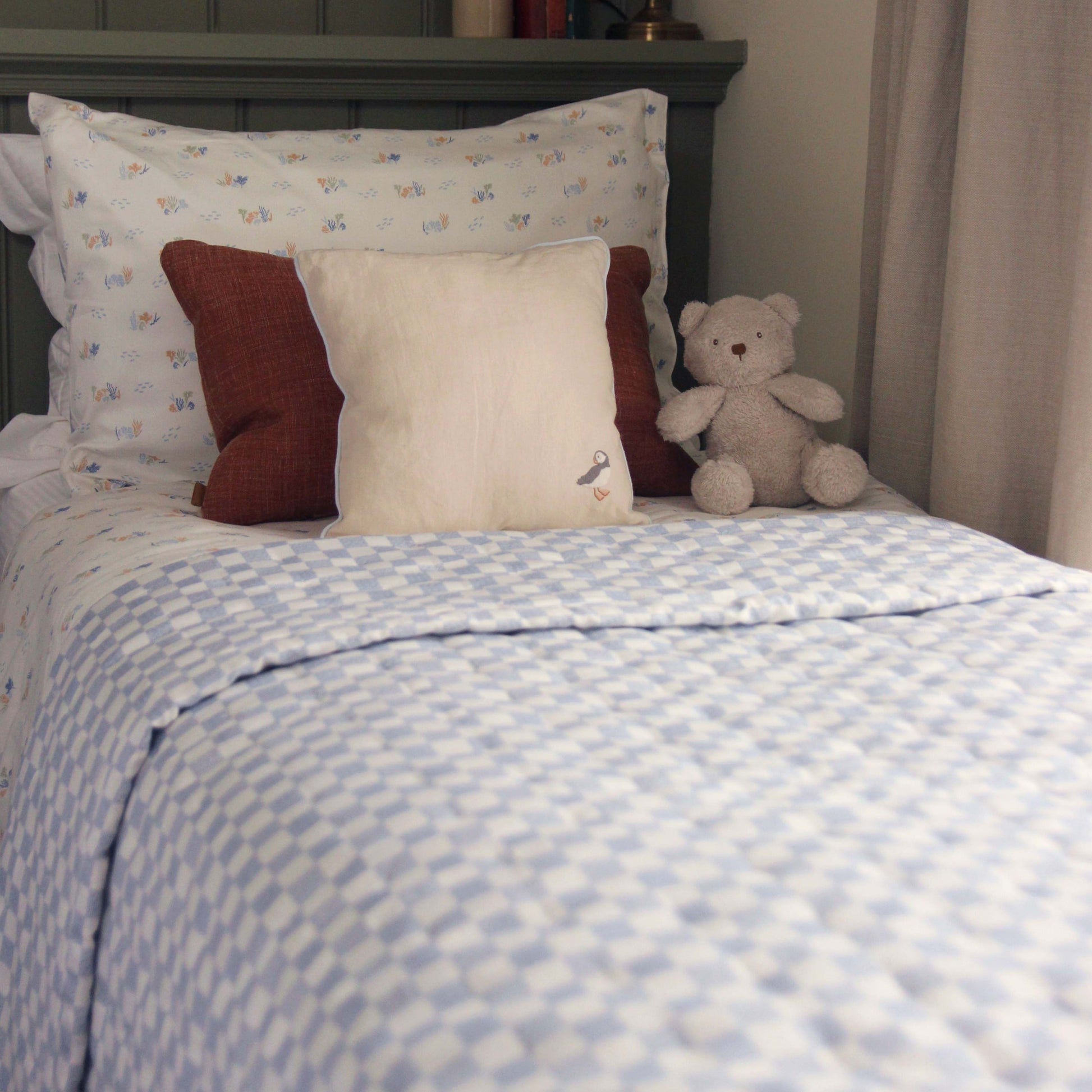 Children's bedroom with a bed featuring patterned bedding, pillows, and a teddy bear.