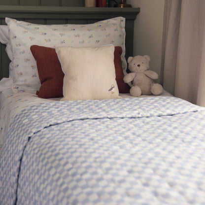 Children's bedroom with a bed featuring patterned bedding, pillows, and a teddy bear.