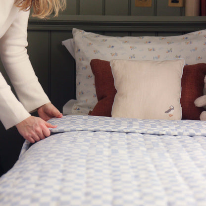 Person making a bed with patterned and solid-colored pillows.