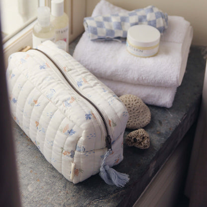 Quilted toiletry bag with floral pattern on a bathroom counter with towels and bottles.