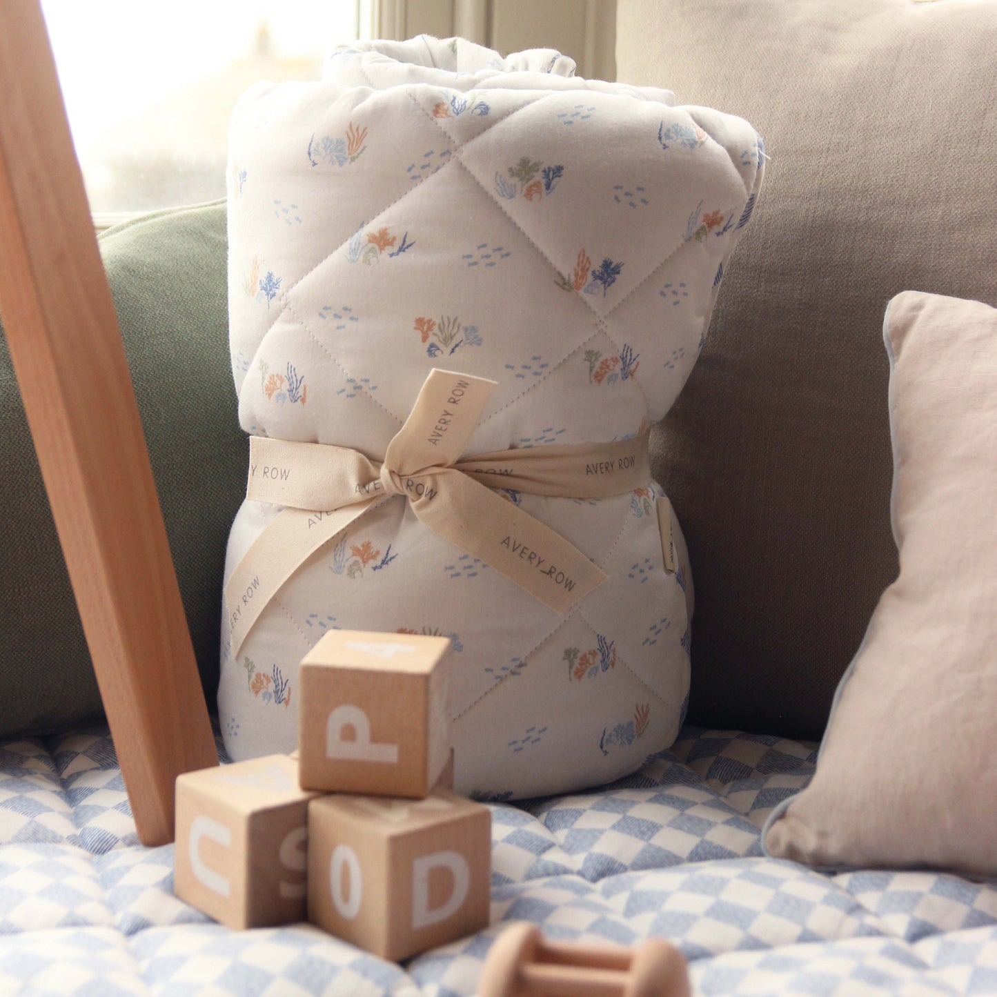 Baby swaddle with floral pattern on a crib with wooden blocks and a pillow.