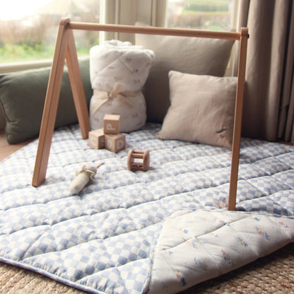Children's play area with a wooden play gym, soft mat, and toys in a room with large windows.