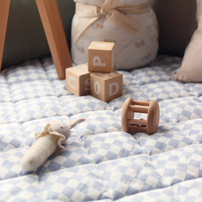 Wooden blocks with letters, a plush toy, and a wooden rattle on a checkered blanket.