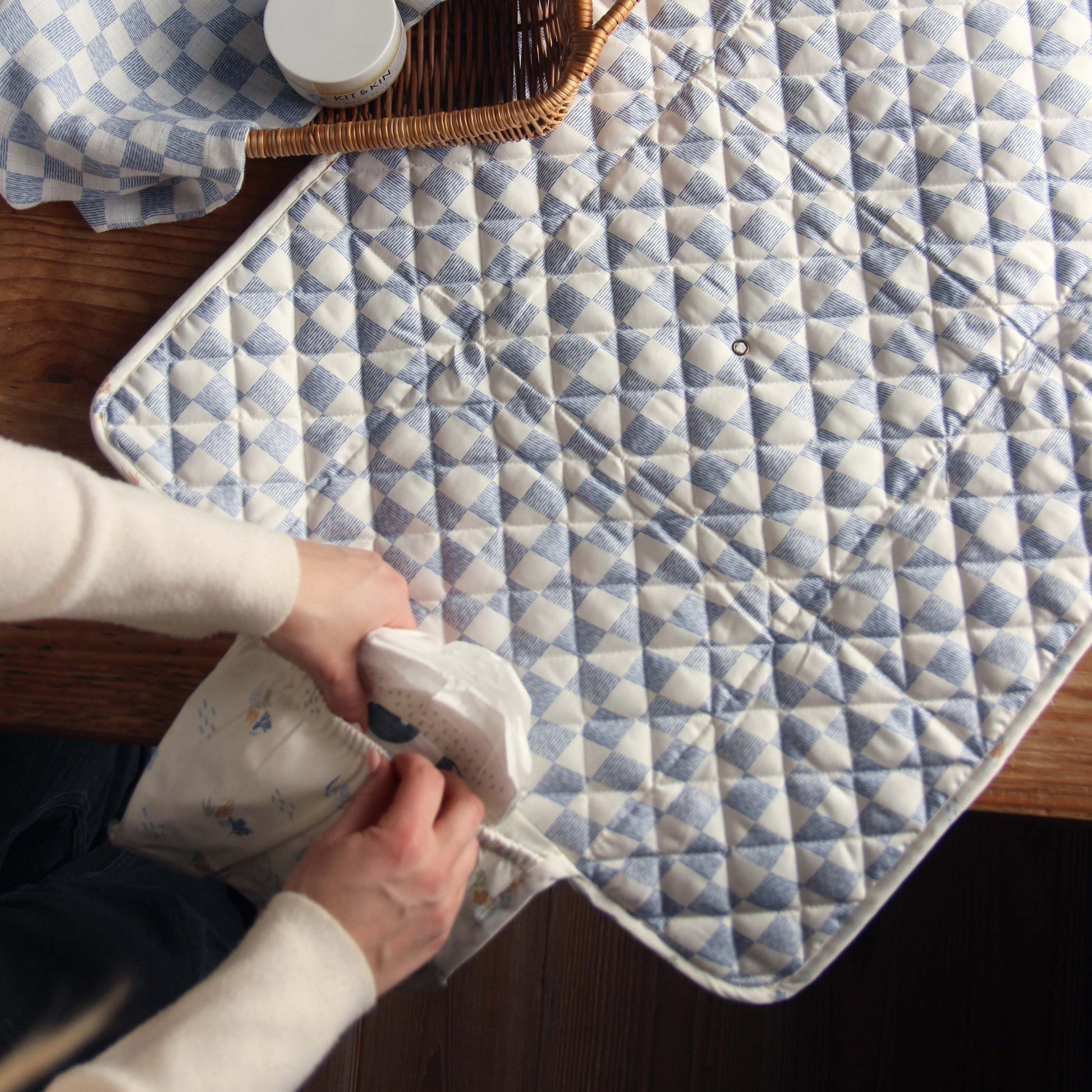 Person holding a white container over a blue and white checkered quilt on a wooden surface.