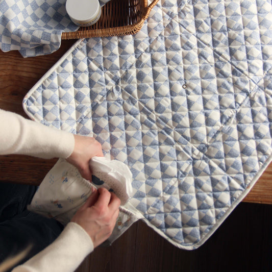 Person holding a white container over a blue and white checkered quilt on a wooden surface.