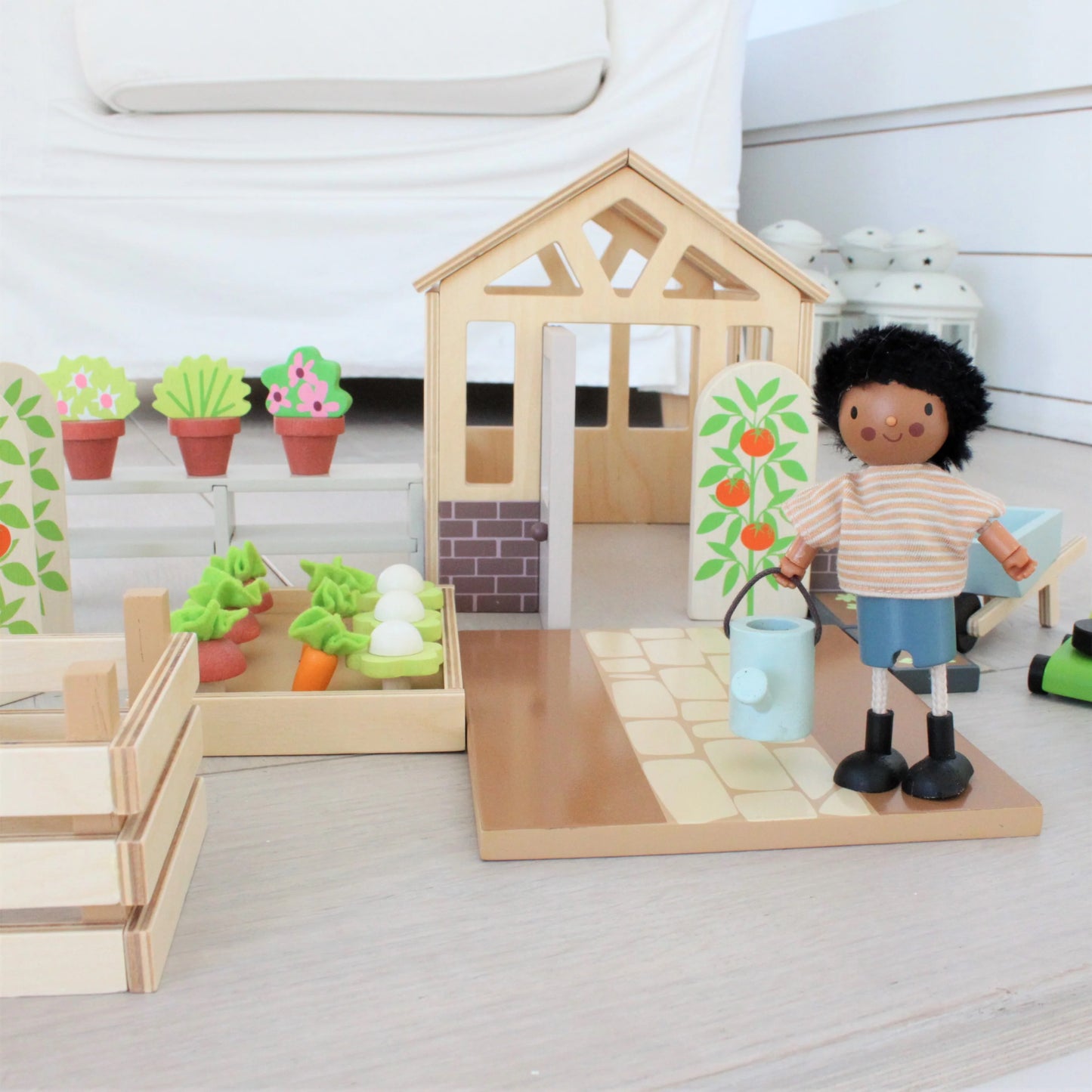 Wooden playset with a house, garden, and toy figure on a light surface.