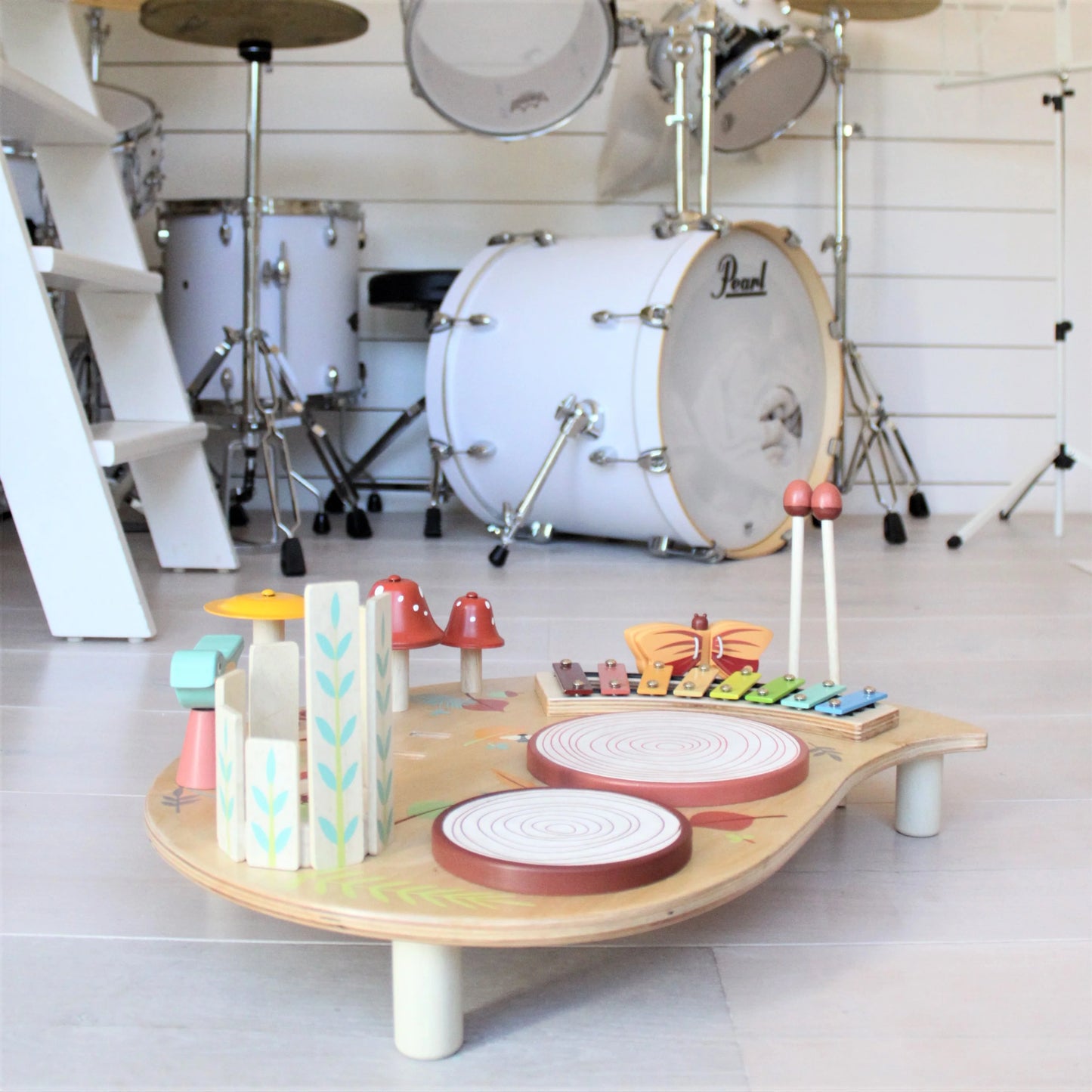 Children's musical toy set on a stand with a full-sized drum set in the background.
