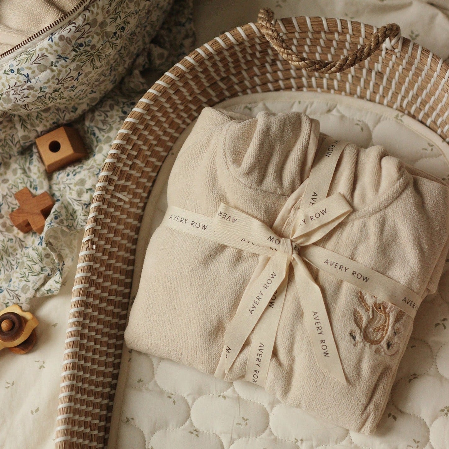 Folded baby outfit with 'Avery Row' branding on a textured surface with toys and a basket.