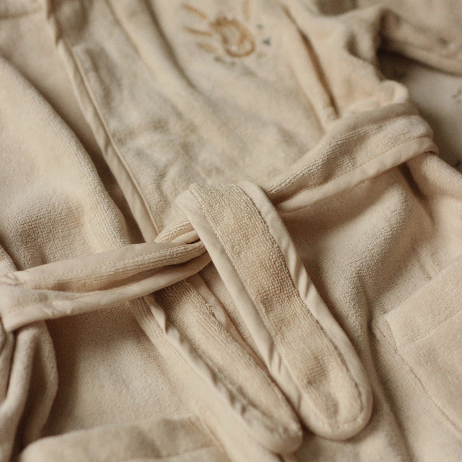 Close-up of a beige robe with a tie, featuring soft texture and embroidery.