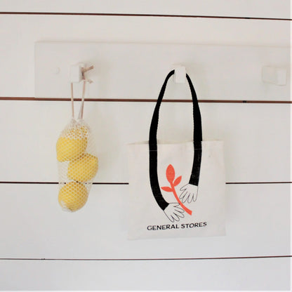 Tote bag with a design of two hands holding a branch, labeled 'General Stores', on a wooden surface.