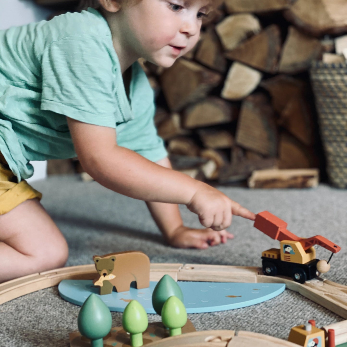 Child playing with wooden toy train set on a carpeted floor.