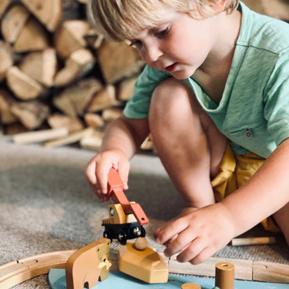Child playing with a wooden toy train set on the floor.