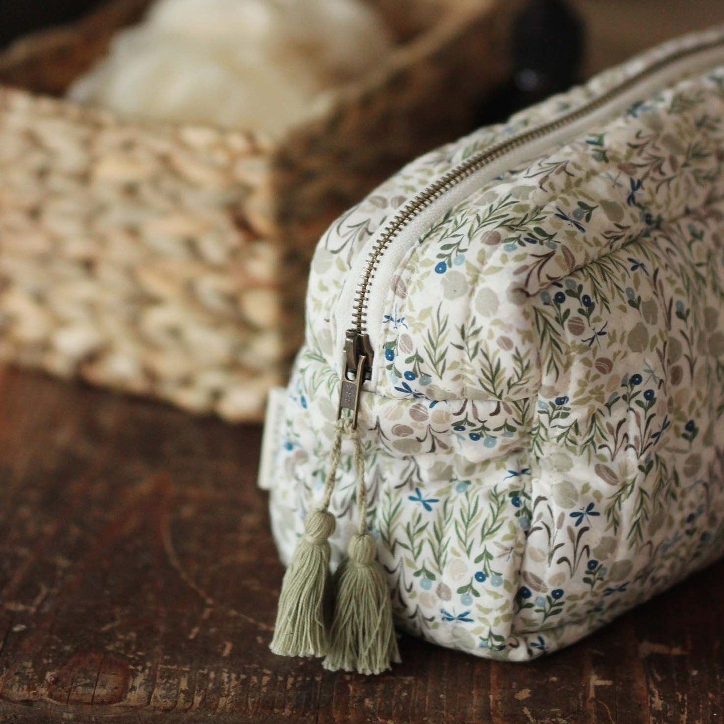 Floral-patterned toiletry bag with a tassel on a wooden surface