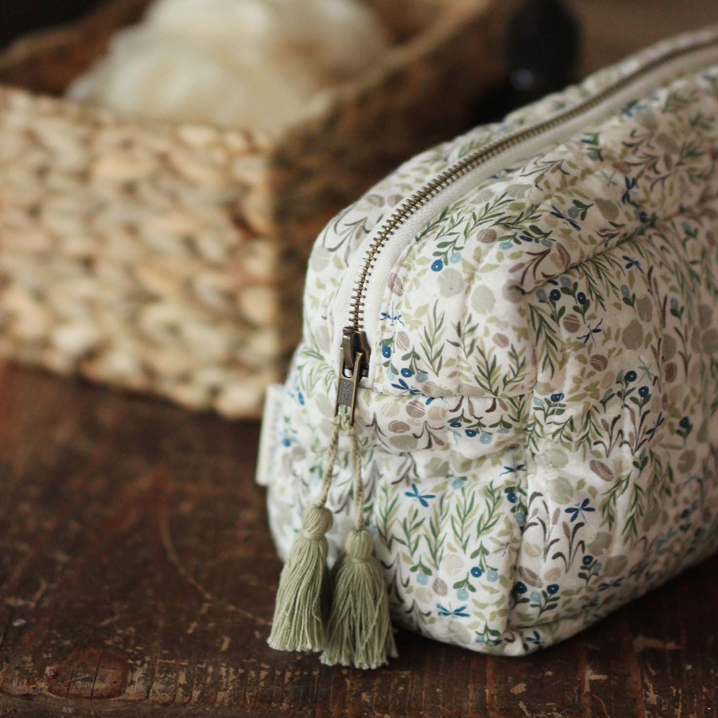 Floral-patterned toiletry bag with a tassel on a wooden surface