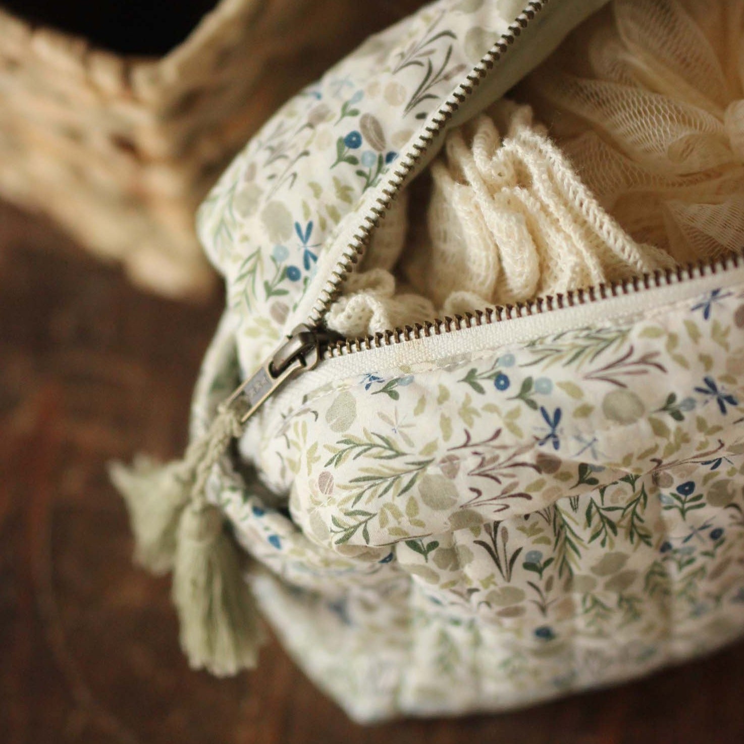 Floral-patterned bag with a zipper, containing beige fabric and tassels.