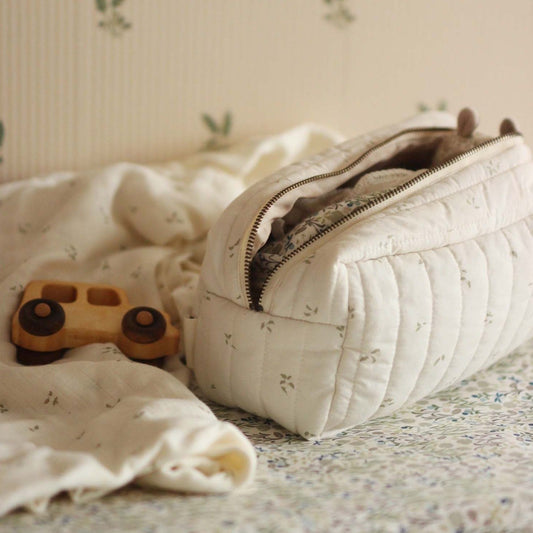 Quilted toiletry bag on a floral bedspread with a wooden toy car nearby