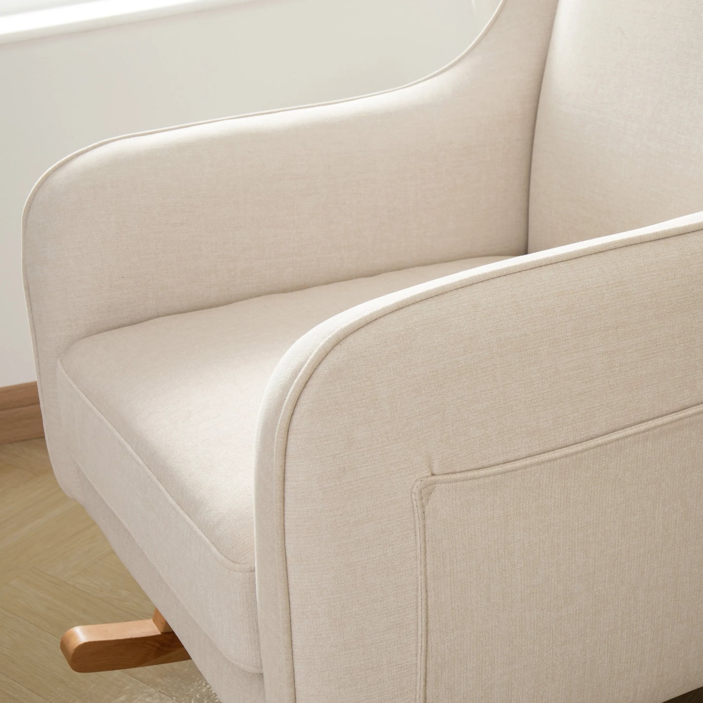 Close-up of a beige upholstered chair with wooden armrests on a light wooden floor.