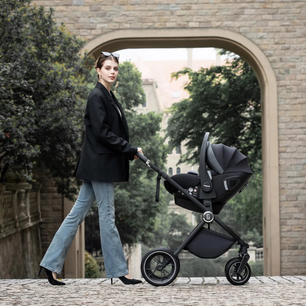 Woman pushing a black stroller in an urban setting with trees and a building in the background.