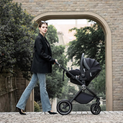 Woman pushing a black stroller in an urban setting with trees and a building in the background.