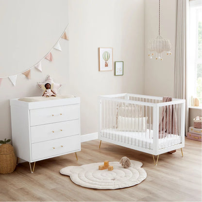 Nursery room with white crib and dresser on a wooden floor.