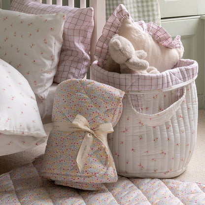 Baby nursery with patterned pillows, a basket, and a baby bonnet on a bed.