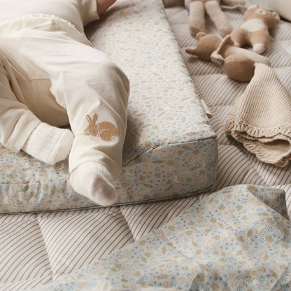 Baby's legs in white pants with a bunny logo on a floral-patterned couch.